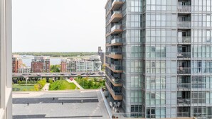 Een modern hooggebouw met meerdere balkons en grote ramen, met uitzicht op een stadsgezicht met een rivier en een brug.