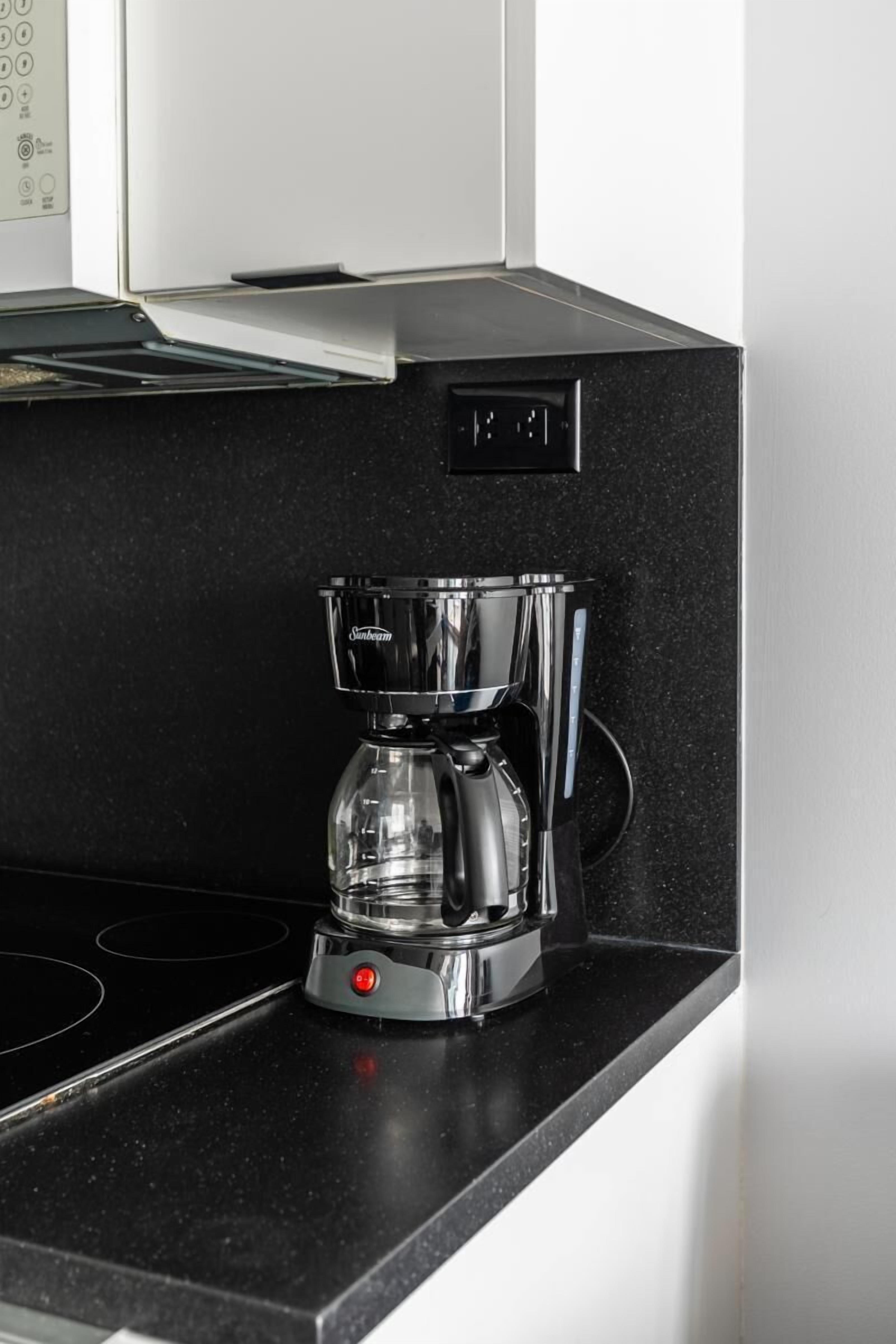 Una cocina moderna con encimera negra, cafetera de acero inoxidable y placa de cocina negra.