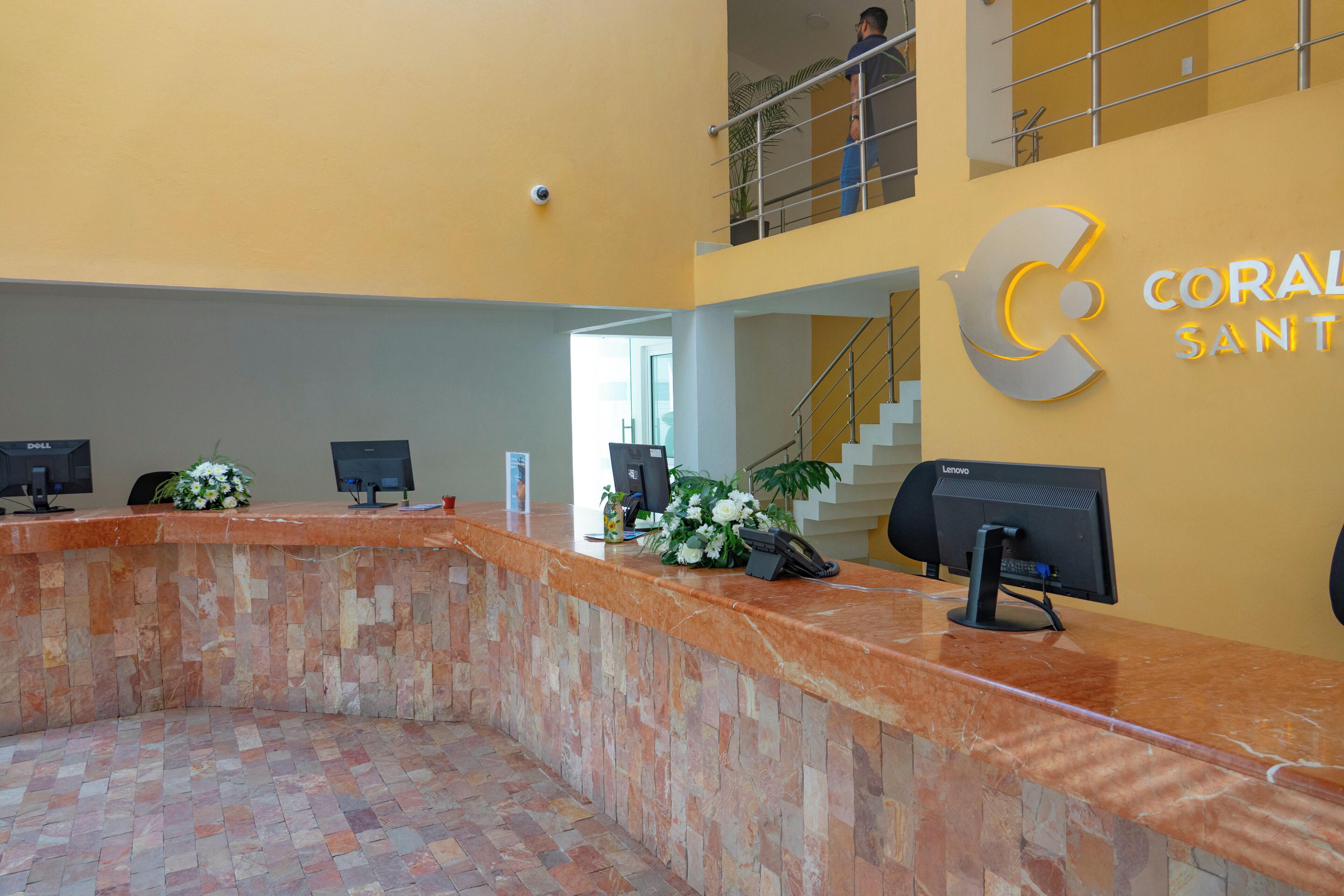 A reception desk with multiple computer monitors, a flower arrangement, and a staircase leading to an upper level.