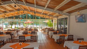 Un restaurante espacioso con varias mesas y sillas, amplias ventanas y techo de madera.
