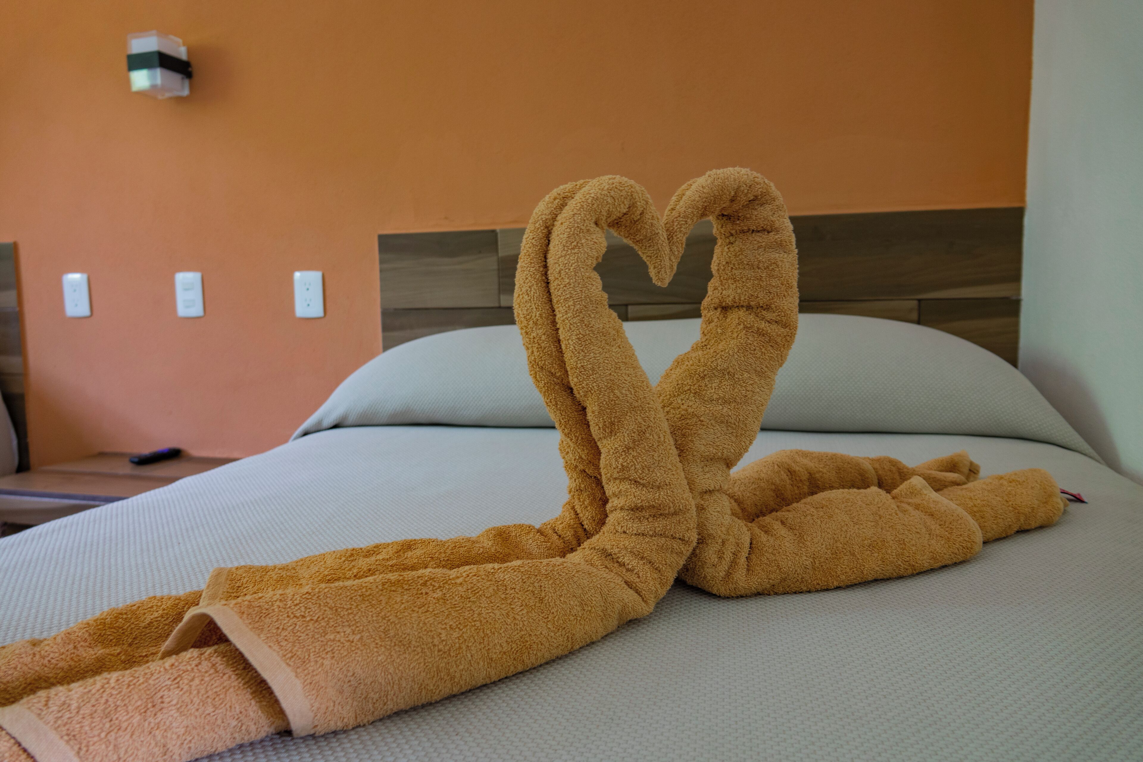 A bed with a towel arranged in a heart shape on the bed.