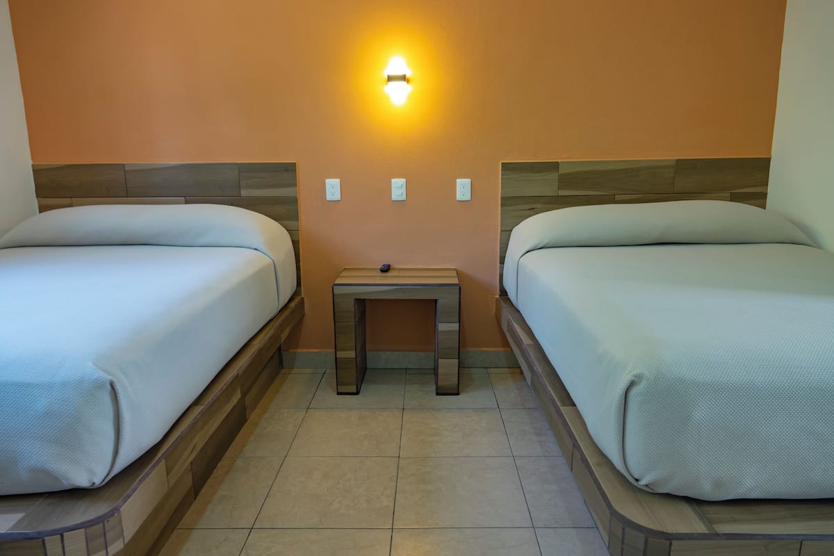 Habitació d'hotel amb dos llits, una tauleta de nit i una làmpada de paret.