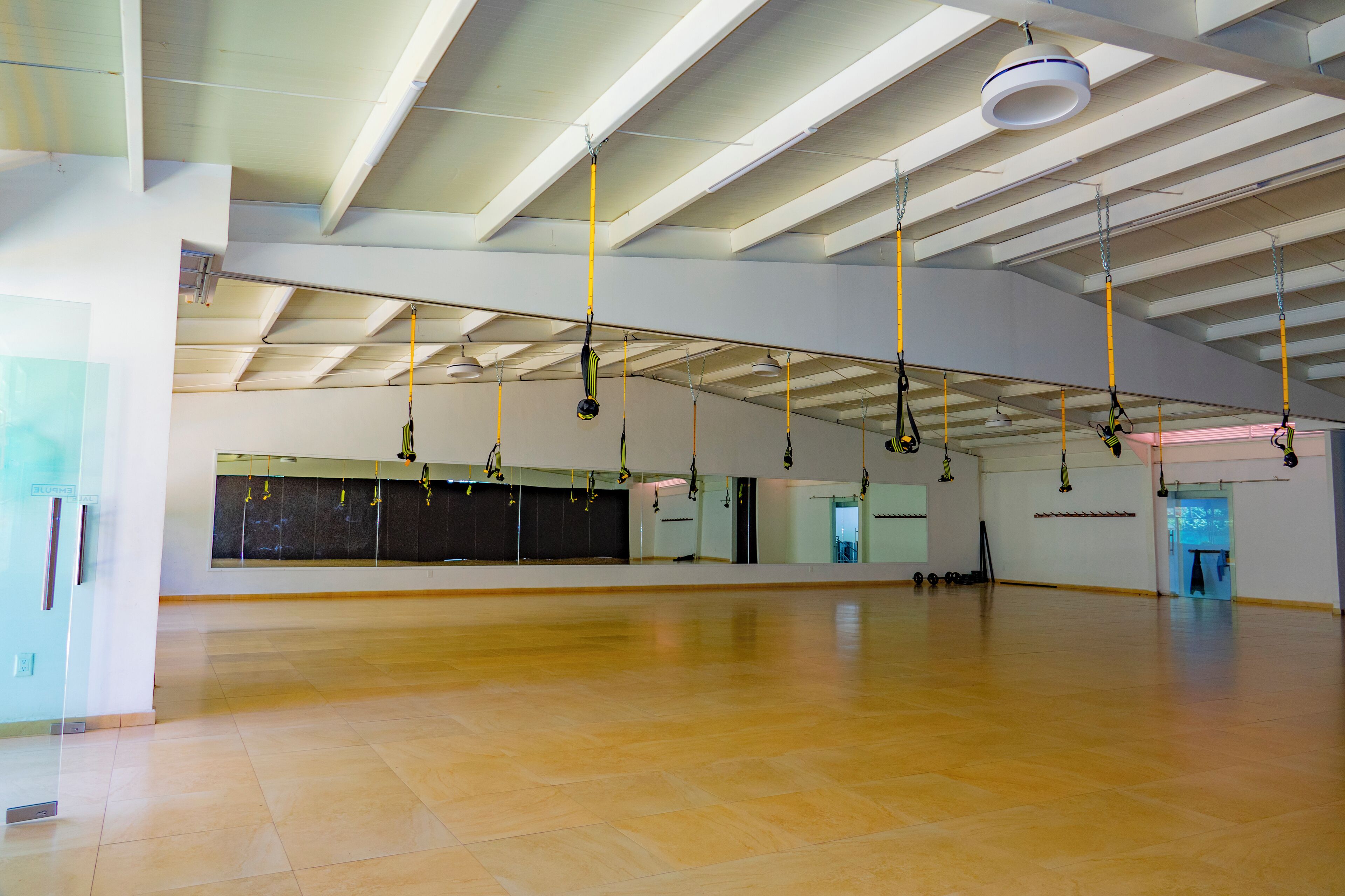 Una habitación amplia con suelo de madera, espejos grandes y equipo de ejercicio colgado.