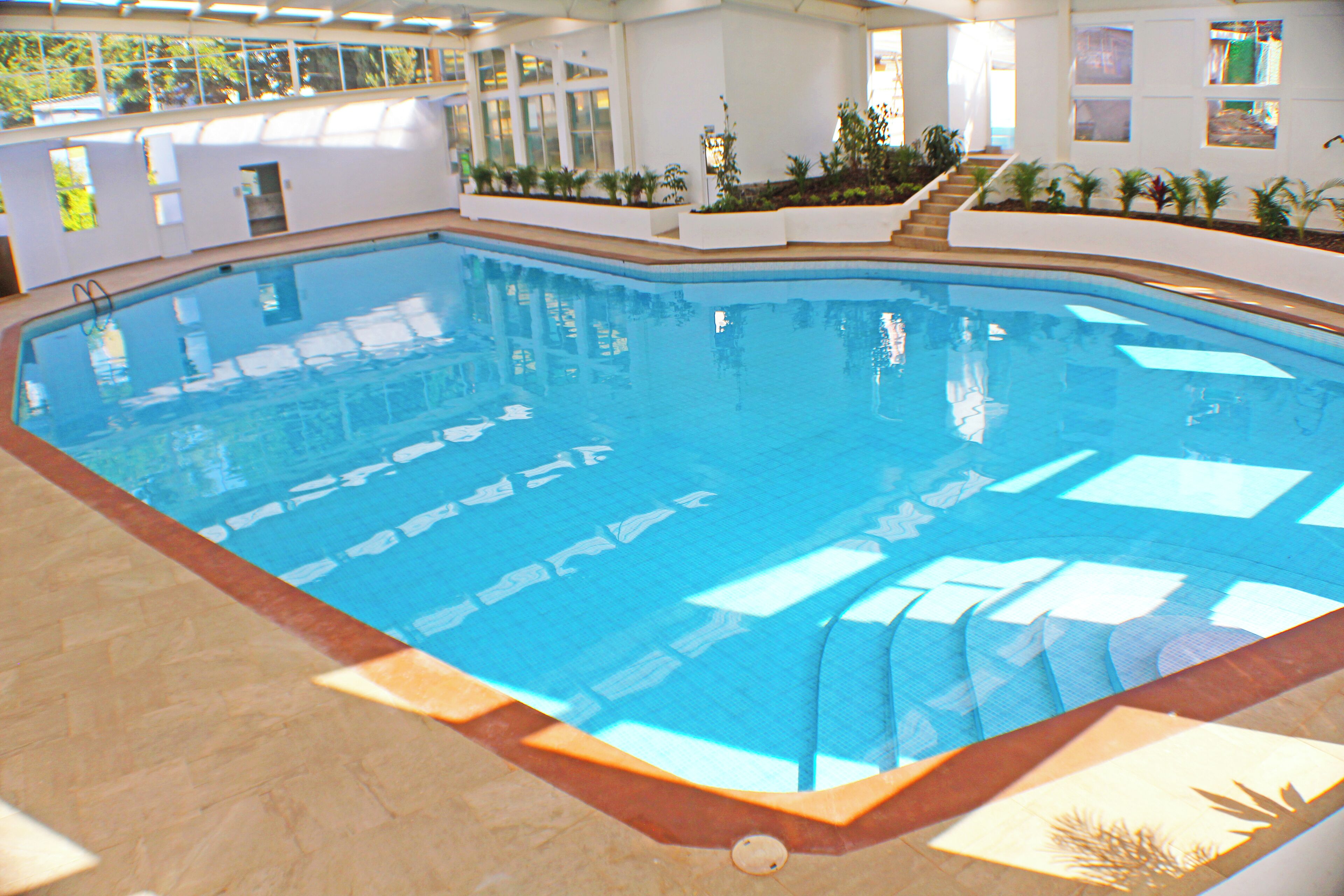 An indoor swimming pool with clear water, surrounded by white walls and a tiled floor.