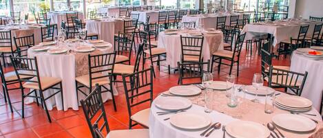 A restaurant with round tables, white tablecloths, and black chairs.