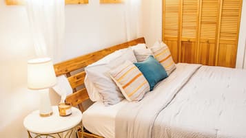 Uma cama bem arrumada com almofadas listradas, uma mesa de cabeceira com abajur e uma cabeceira de madeira.