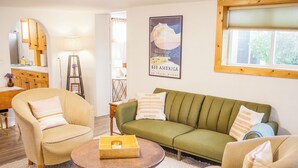 A living room with a green sofa, beige armchairs, a wooden coffee table, and a framed poster on the wall. - Charming Casita - 3 BDRM Downtown (Bozeman)
