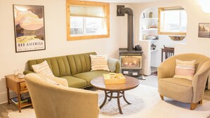 A cozy living room with a green sofa, beige armchairs, a coffee table, and a wood-burning stove. - Charming Casita - 3 BDRM Downtown (Bozeman)