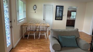A living room with a grey sofa, a wooden dining table with white chairs, a white door, and a wall clock.