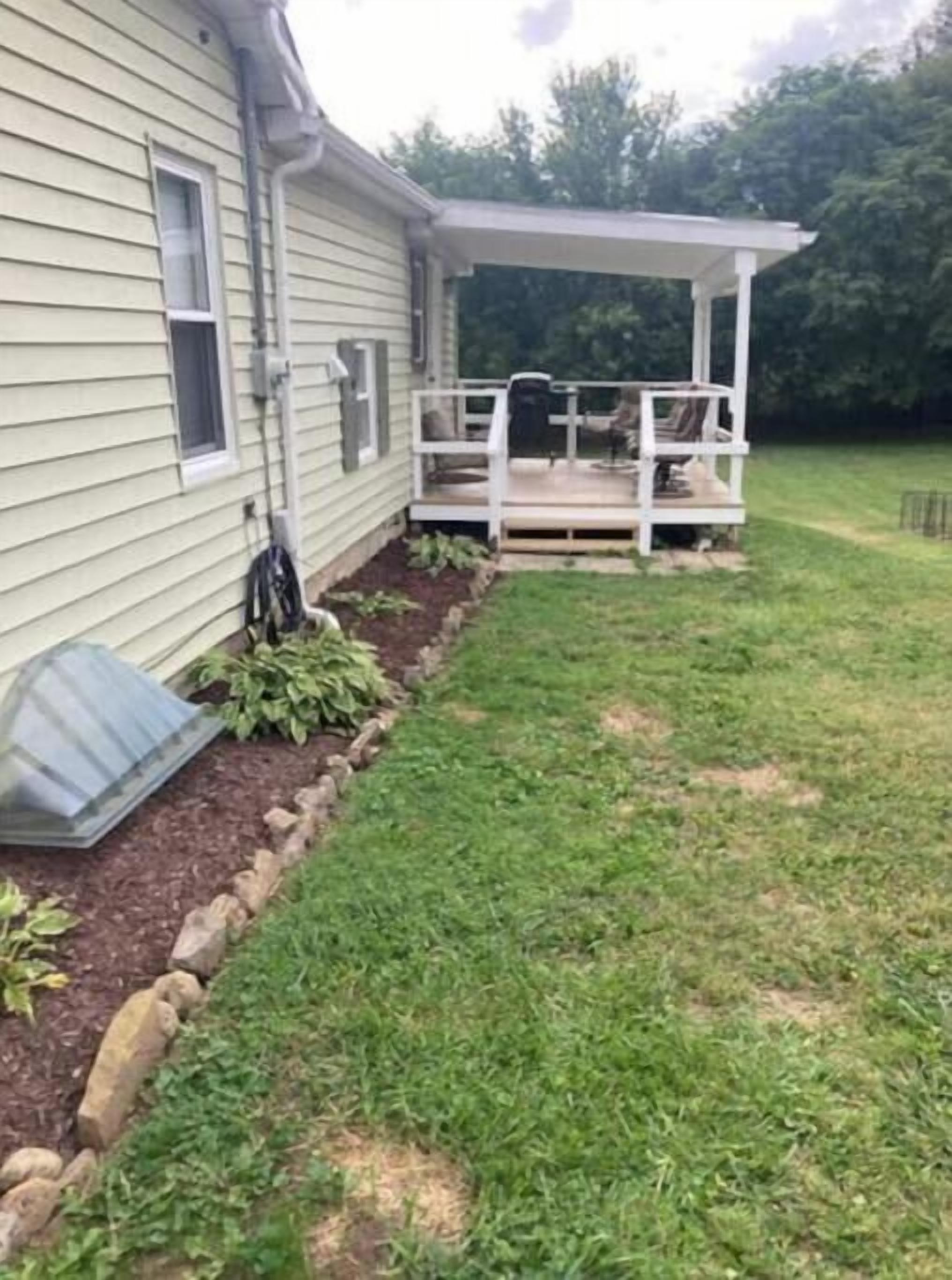 A house with a covered porch, a window, and a garden area with mulch and plants.
