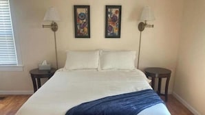 A bedroom with a large bed, two nightstands, two wall-mounted lamps, and two framed floral paintings. - Cozy city cottage, one floor, covered porches, quiet neighborhood  (Newark)