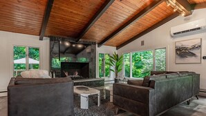 Un salon moderne doté d’une cheminée, de sièges confortables et de grandes fenêtres offrant une vue sur la verdure.