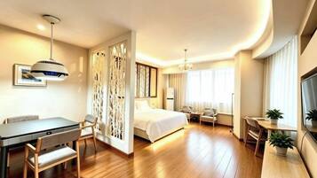 A hotel room with a bed, a desk with chairs, a dining table, and a TV.