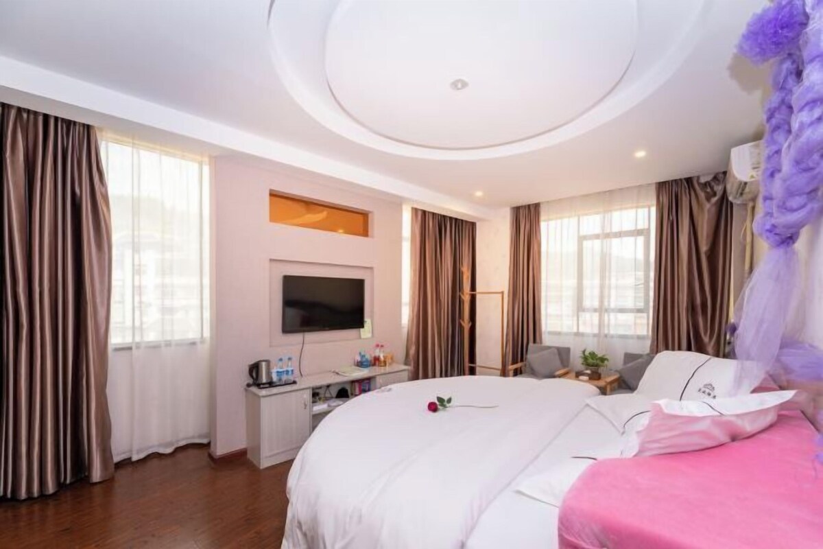 Une chambre d’hôtel avec un grand lit, une télévision, un bureau avec un ordinateur et une fenêtre avec des rideaux.