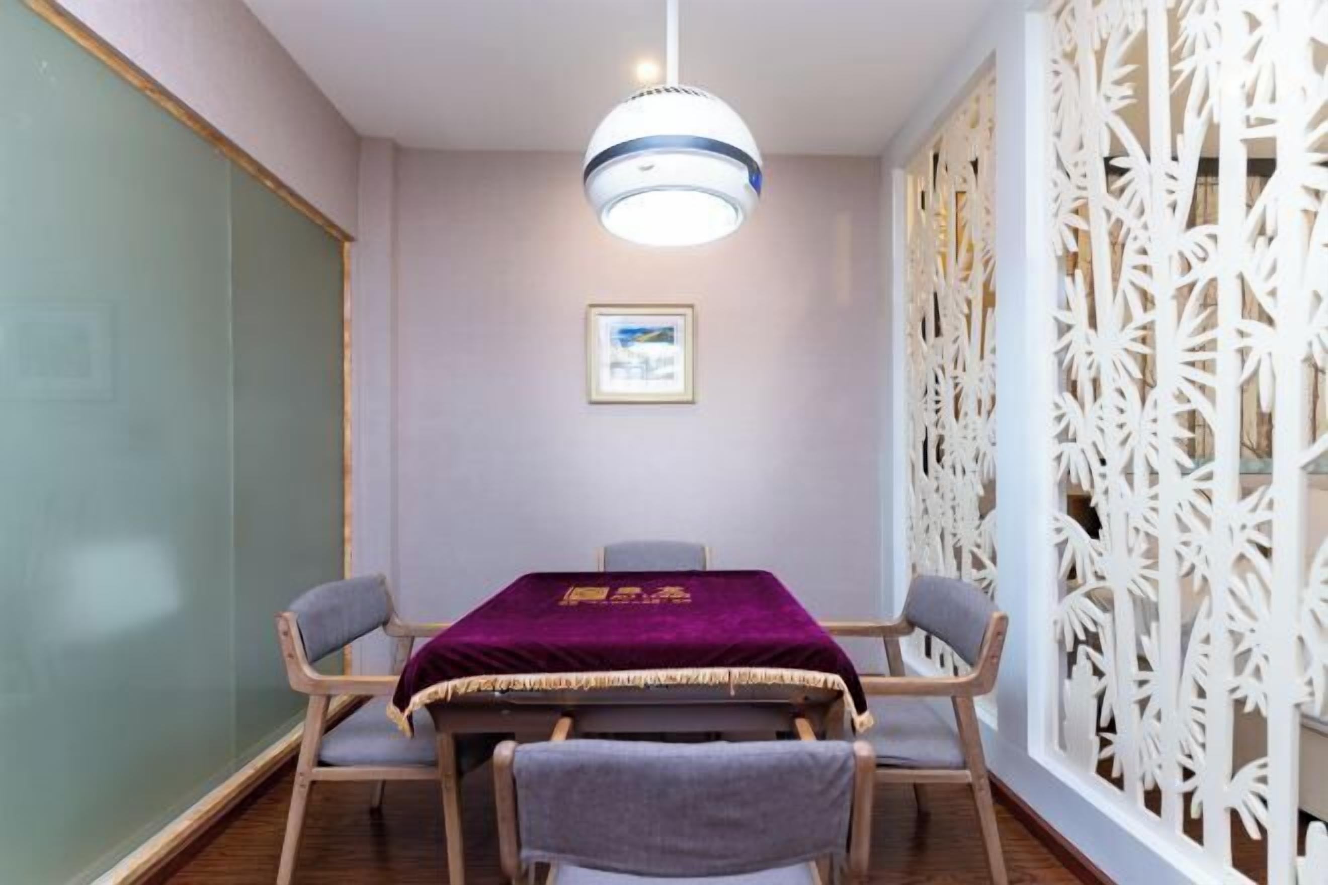 Un salón de conferencias con una mesa, sillas, una lámpara colgante, un separador decorativo y un cuadro en la pared.