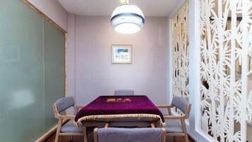 Un salón de conferencias con una mesa, sillas, una lámpara colgante, un separador decorativo y un cuadro en la pared.