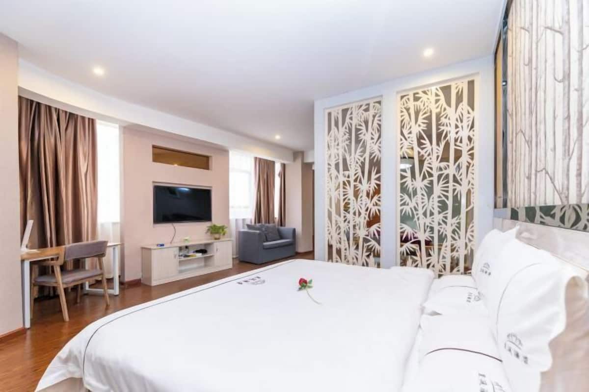 Ein Hotelzimmer mit einem großen Bett, einem Fernseher, einem Schreibtisch mit Stuhl und einem dekorativen Raumteiler.