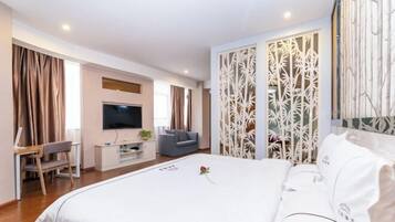 Una habitación de hotel con una cama grande, un televisor, un escritorio con una silla y un separador decorativo.
