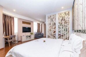Une chambre d’hôtel avec un grand lit, une télévision, un bureau avec une chaise et un élément de séparation décoratif.