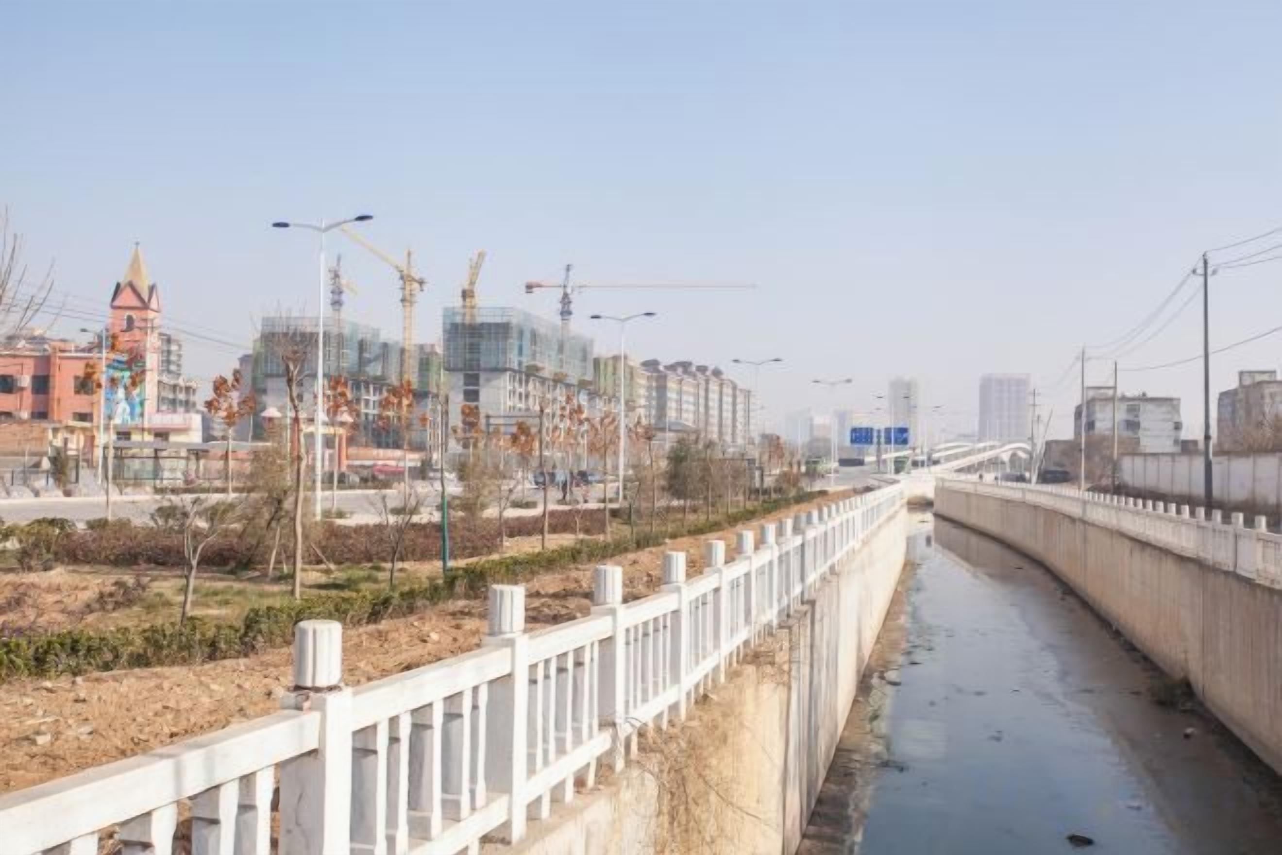 Een rivier die langs een brug stroomt, met bouwkranen en gebouwen op de achtergrond.