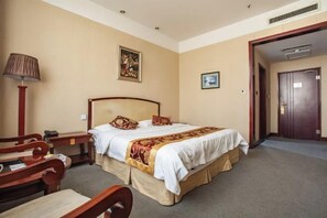 Een hotelkamer met een groot bed, een bureau met een lamp en een deur naar een andere kamer.