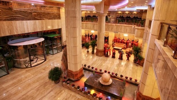 A hotel lobby with marble flooring, large columns, a central fountain, and a seating area with red decor. - Taoyuan International Hotel (Yuncheng)