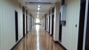 A long, narrow hallway with a shiny floor, doors on both sides, and a fire extinguisher on the right wall. - Taoyuan International Hotel (Yuncheng)