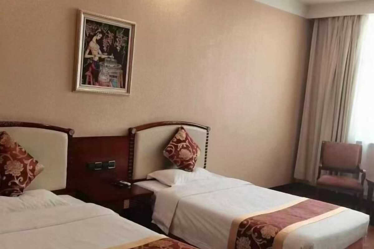 Une chambre d’hôtel avec deux lits, un tableau au mur, une chaise et une fenêtre avec des rideaux.