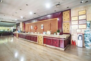 Un área de recepción con piso de mármol, una mesa de recepción con paneles decorativos, certificados enmarcados en la pared y un dispensador de agua.
