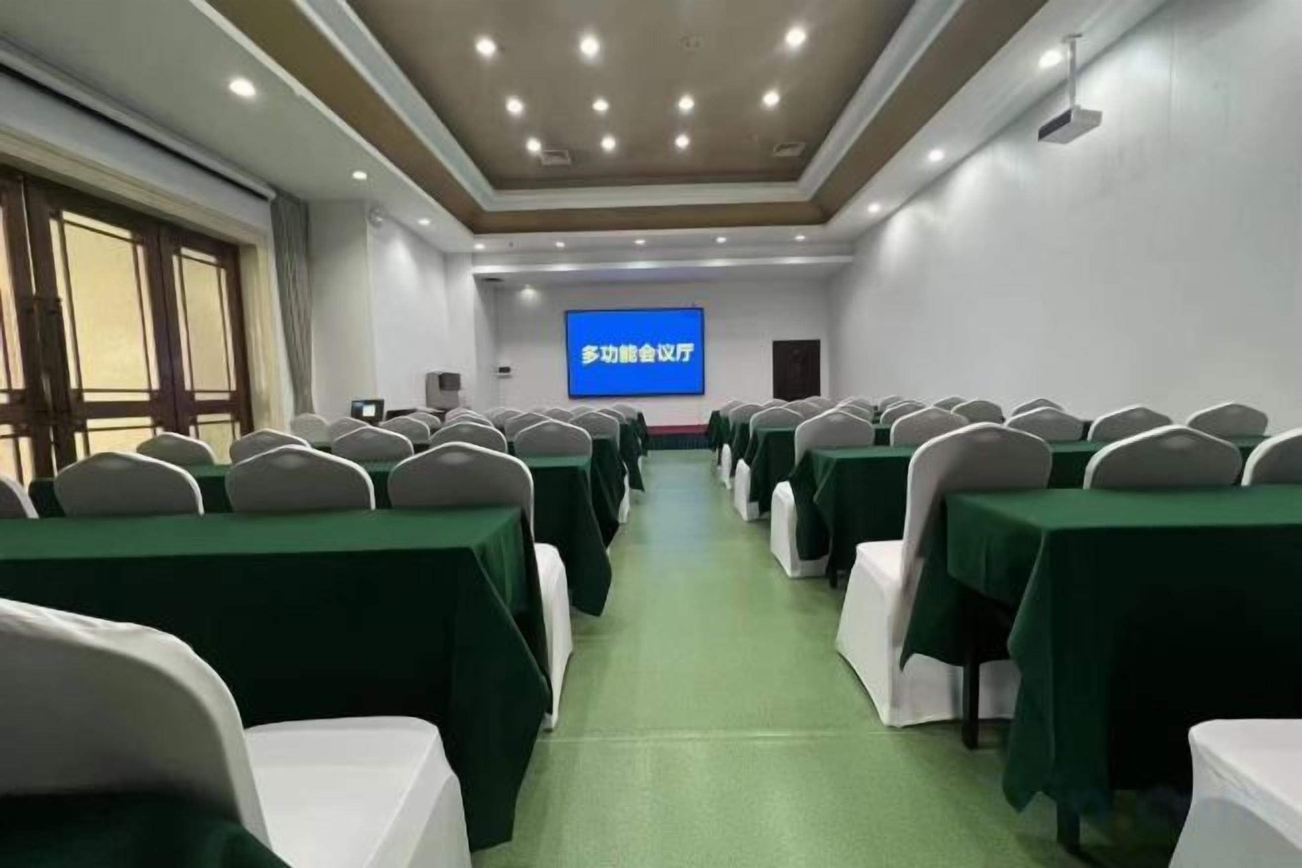 A conference room with rows of tables and chairs, a projection screen, and a green carpet.