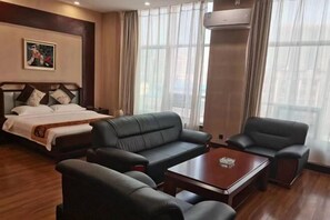 Una habitación de hotel con una cama, un sofá, dos sillones, una mesa de centro y un cuadro en la pared.