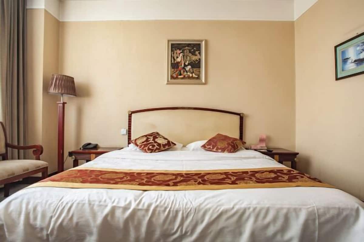 Une chambre d’hôtel avec un grand lit, une tête de lit en bois, une table de chevet avec une lampe et un tableau encadré au mur.