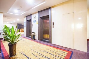 Un hall d’hôtel avec un comptoir d’accueil, deux ascenseurs et une plante en pot.