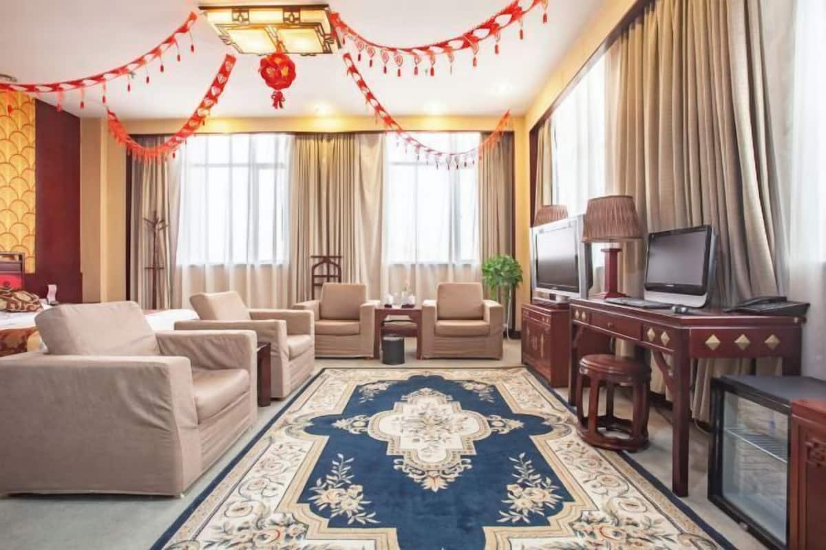 Une chambre d’hôtel avec un grand tapis bleu à motifs, des canapés beiges, une télévision et des rideaux.