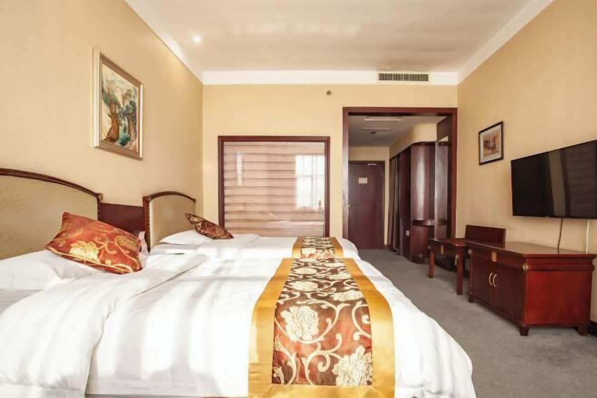 Une chambre d’hôtel avec un grand lit, une commode en bois, une télévision et une porte donnant sur une autre pièce.