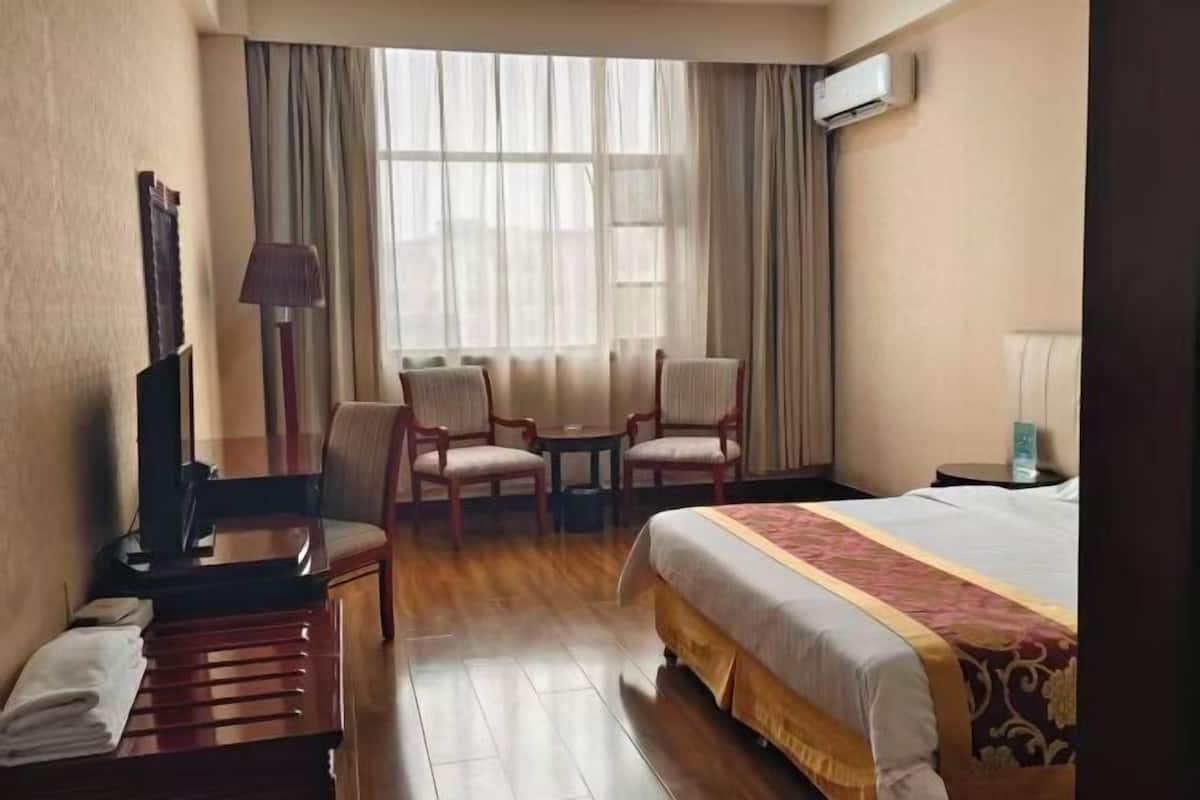 Une chambre d’hôtel équipée d’un lit, d’un bureau, d’une chaise, d’une petite table et d’une fenêtre avec des rideaux.