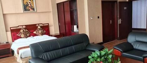 Habitación de hotel con cama, sofá de cuero negro, una mesita de centro de madera con una planta, un armario y una puerta.