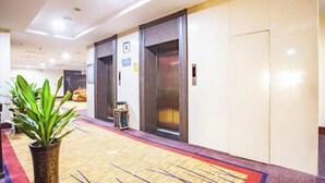A hotel lobby with two elevators, a potted plant, and a carpeted floor. - Taoyuan International Hotel (Yuncheng)
