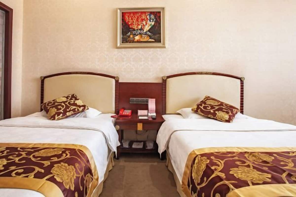 Une chambre d’hôtel avec deux lits, chacun doté d’une tête de lit et d’une couvre-lit décorative. On y trouve un petit bureau avec un téléphone et, au mur au-dessus, un tableau encadré.