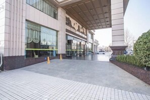 Ein Hotel mit überdachter Eingangspforte, Glastür und Parkplatz.