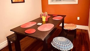 Un coin repas avec une table en bois foncé, des sets de table rouges et un lustre.