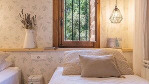 A bedroom with a wooden window, a bedside table with a vase of flowers, a hanging light fixture, and a bed with two pillows. - La Casa 1950 Montefrío by Ruralidays (Granada)