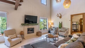 A spacious living room with a fireplace, comfortable seating, a flat-screen TV, and a large window offering a view of greenery. - La Casa 1950 Montefrío by Ruralidays (Granada)