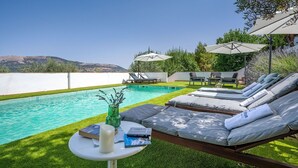 A poolside area with lounge chairs and umbrellas, a small table with books and a candle, and a view of hills in the background. - La Casa 1950 Montefrío by Ruralidays (Granada)
