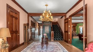 A spacious hallway with a large rug, a chandelier, and a staircase leading to another room. - Luxury Mountain Retreat: Skiing, SPA, Arcade & Bar (Wrightwood)