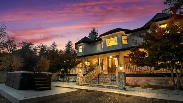 A two-story house with a stone staircase leading to the front door, surrounded by trees and a hot tub in the foreground. - Luxury Mountain Retreat: Skiing, SPA, Arcade & Bar (Wrightwood)