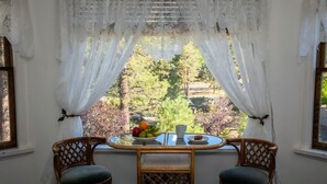 A room with a table and two chairs, a window with white curtains, and a view of trees and foliage. - Luxury Mountain Retreat: Skiing, SPA, Arcade & Bar (Wrightwood)