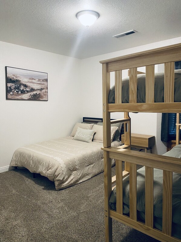 A bedroom with a bunk bed, a single bed, a ceiling light, a wall-mounted air vent, and a framed landscape painting. - Fernwood Retreat at Madera Ranchos (Madera)