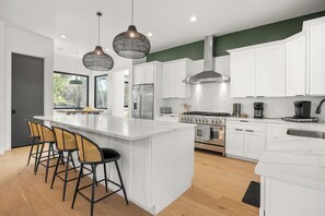 A modern kitchen with white cabinetry, a large island with bar stools, stainless steel appliances, and pendant lighting.