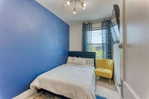 A bedroom with a bed, a chair, and a window with curtains. - Spacious 4BR DC Home | 2 Parking Spots | Sleeps 8 (Washington)
